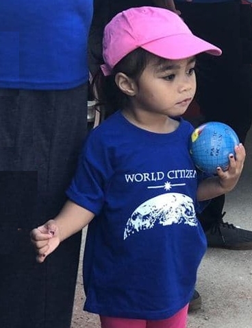 Young child wearing a pink cap & a blue World Citizen T-shirt and carrying a globe ball